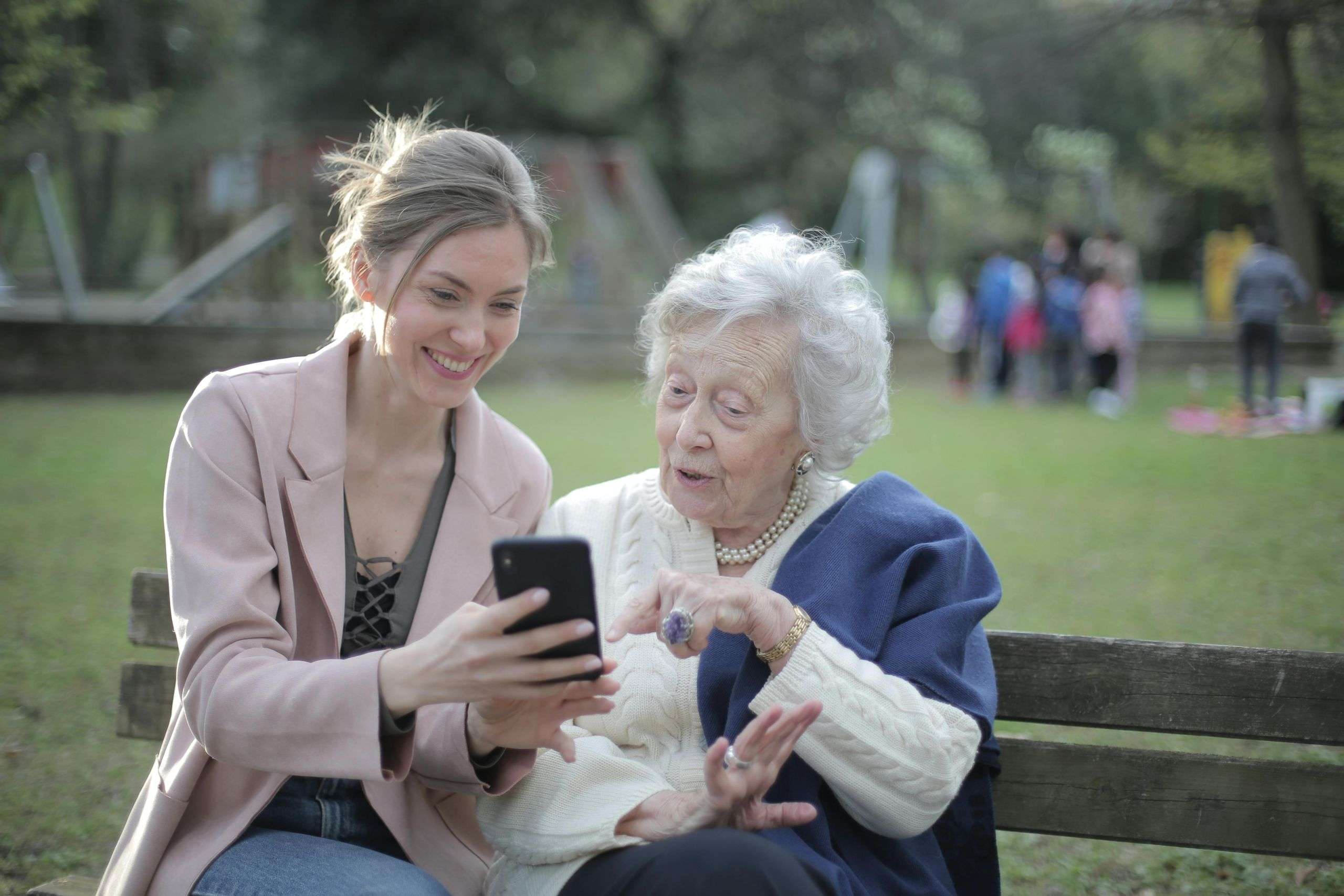 Granddaughter showing her grandmother a phone while sitting on a park bench, symbolizing family support and connection during cremation planning in Tempe Arizona